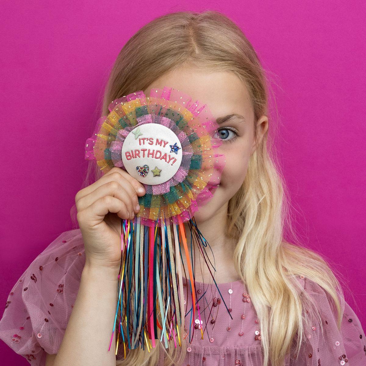 Young girl holding a colorful birthday party hat against a pink background