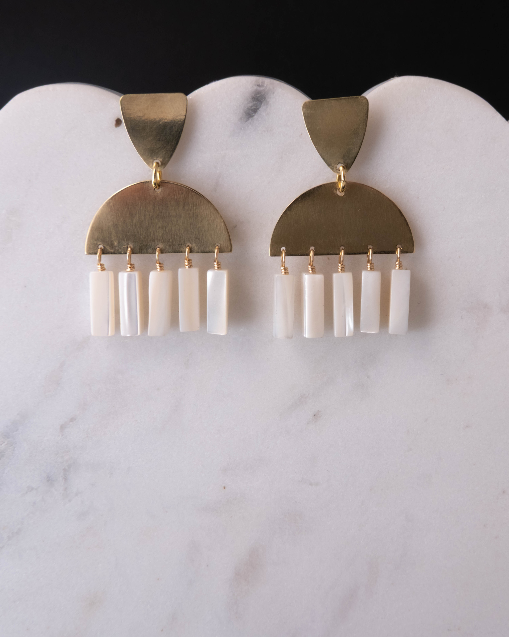Pair of earrings with brass and white mother of pearl design on a marble surface