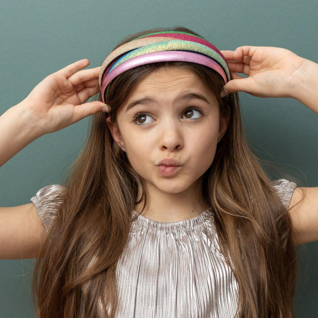 Female presenting child adjusting a colorful headband against a plain background