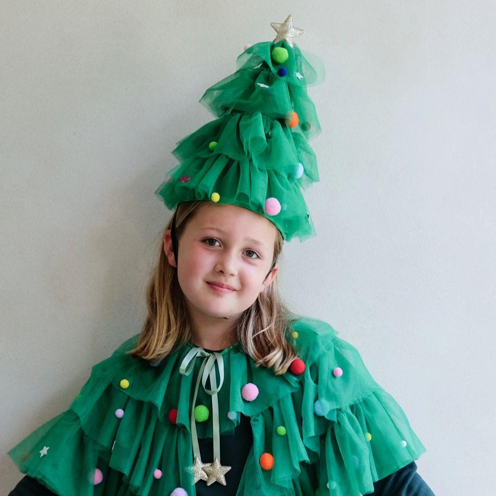Child wearing a green Christmas tree costume with colorful decorations against a plain background