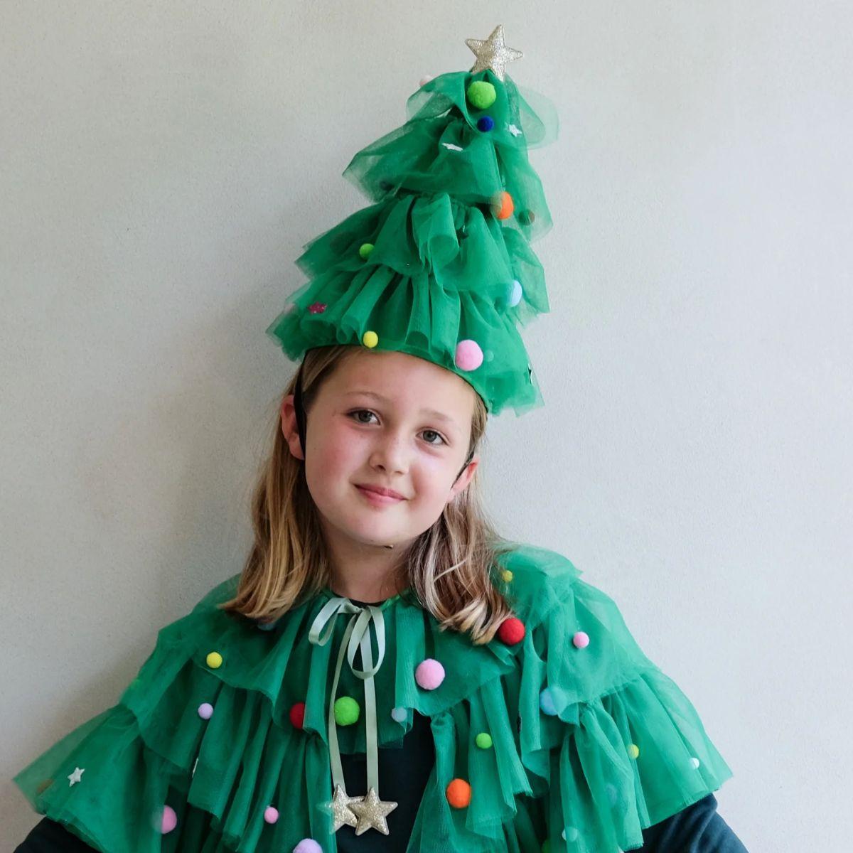 Child wearing a green Christmas tree costume with colorful decorations against a plain background