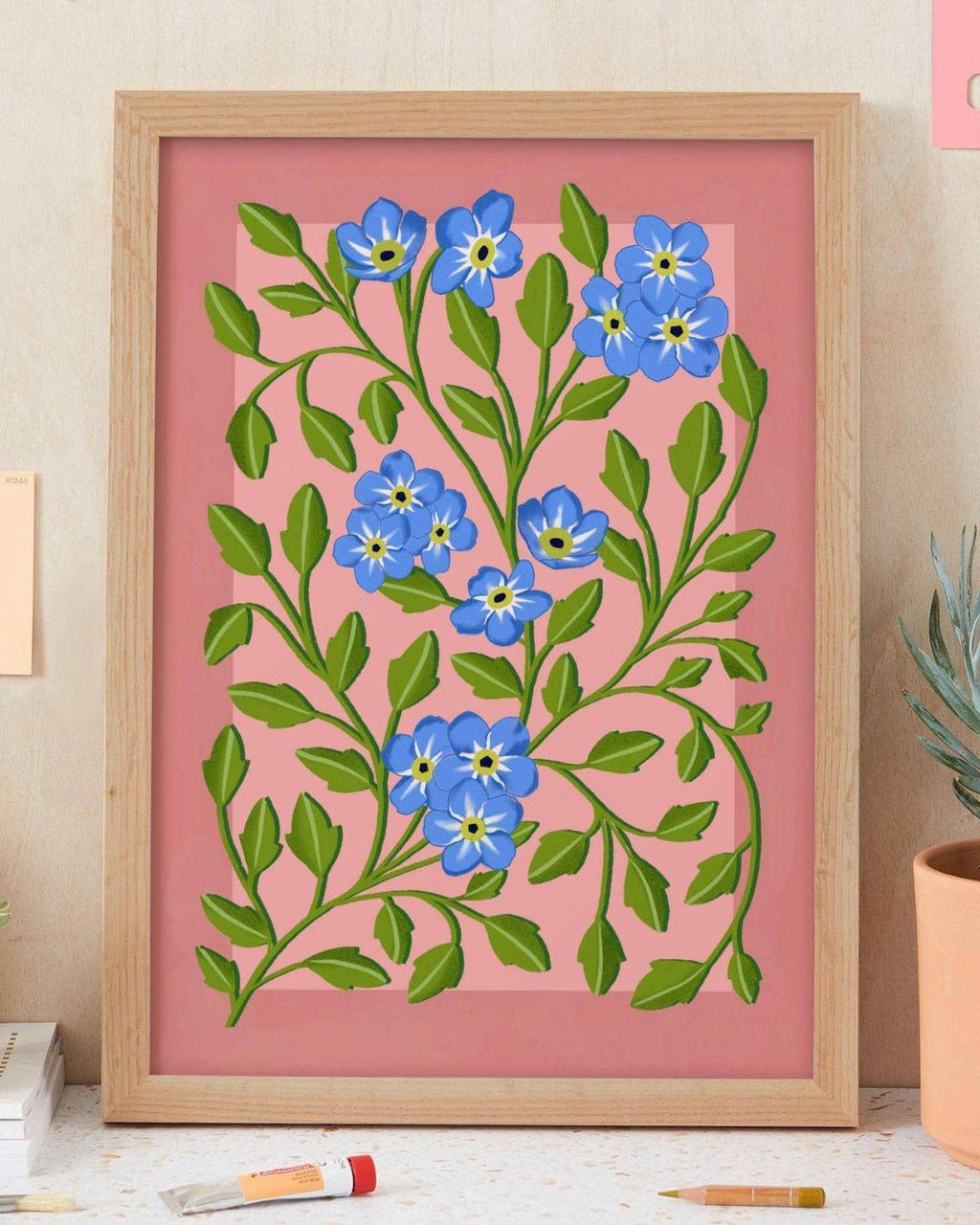 Framed artwork with blue flowers and green leaves on a pink background