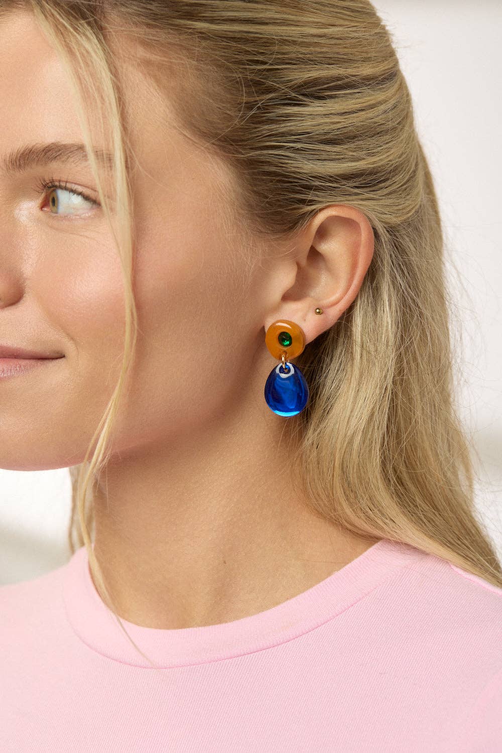 Close-up of a female presenting person wearing colorful earrings with a plain background