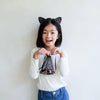 Child wearing black cat ears holding a small bag with a white background
