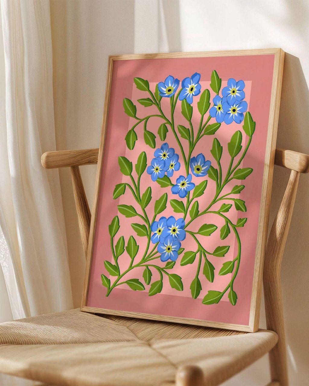 Framed artwork with blue floral design on a pink background, placed on a wooden chair.