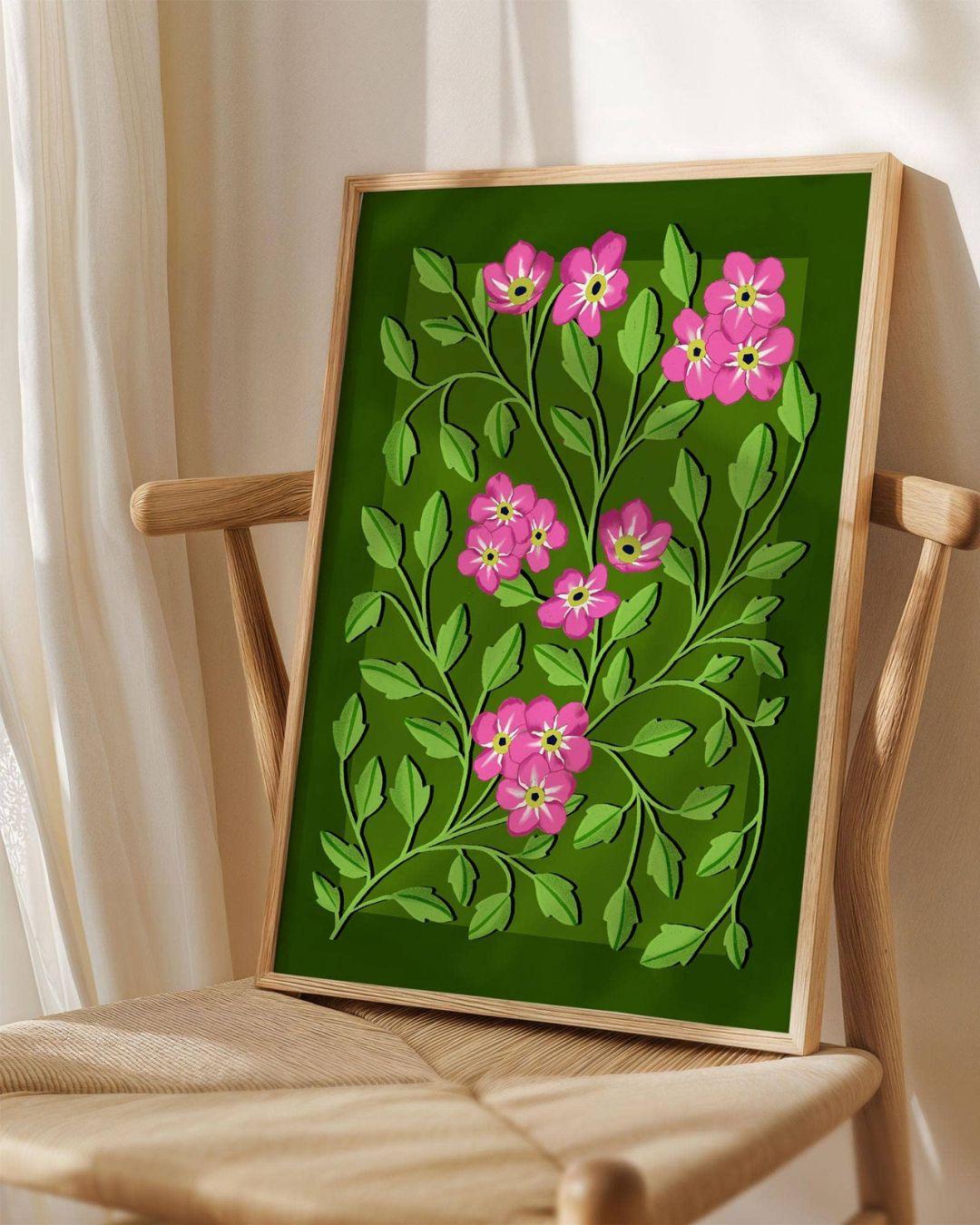 Framed artwork with pink flowers and green leaves on a wooden chair.