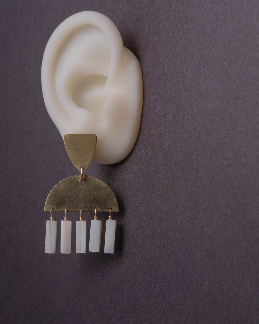 Pair of earrings with brass and white mother of pearl  white ear model against a dark background