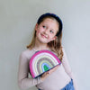 Young girl holding a rainbow-colored pouch against a plain background