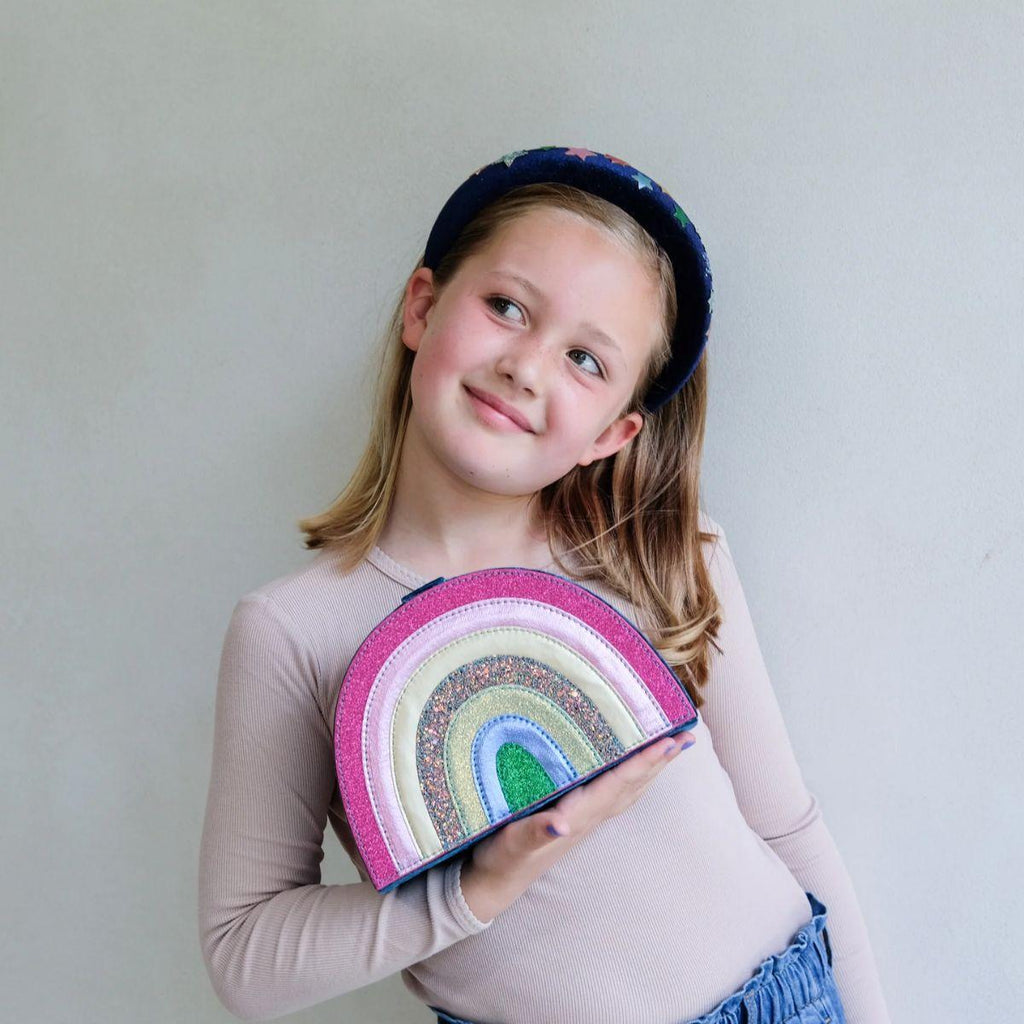 Young girl holding a rainbow-colored pouch against a plain background