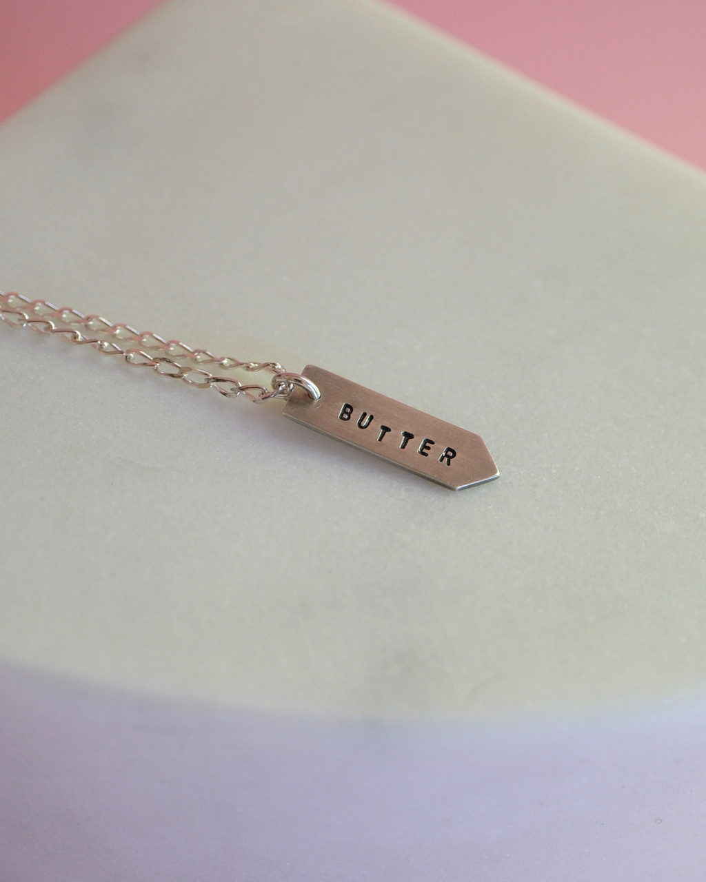 Necklace with a tag that reads 'BUTTER' on a pastel background