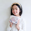 Young female presenting child holding a pouch with a unicorn design against a plain background