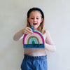 Child holding a rainbow-shaped pouch against a plain background