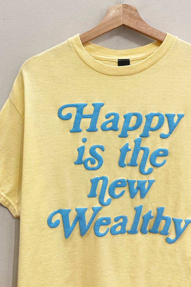 Yellow t-shirt with blue text 'Happy is the new Wealthy' on a hanger against a gray background