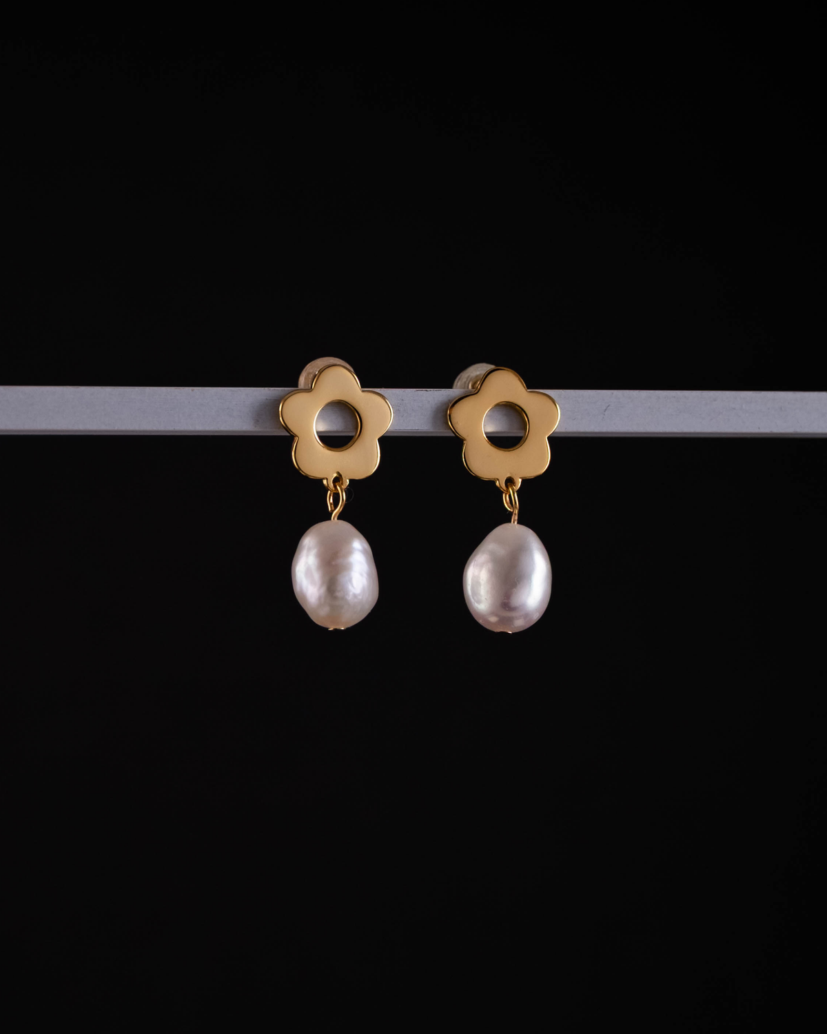 Gold earrings with flower-shaped tops and pearl drops on a black background