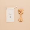 A natural beeswax-coated wooden teething rattle with a label attached reading 'Pǩpi Kiss Teething Rattle', alongside a cotton storage bag.