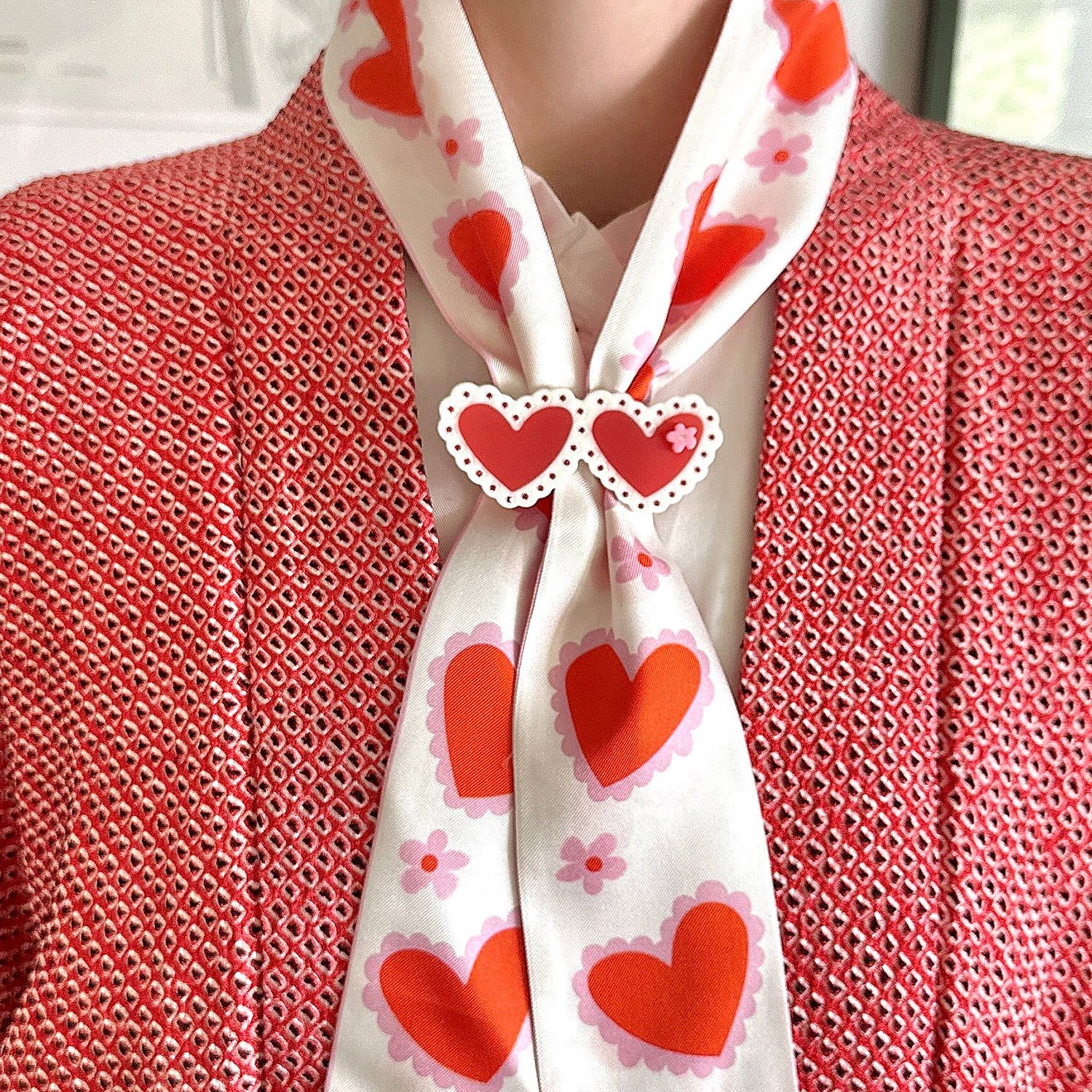 Person wearing a white scarf with red heart patterns over a red textured garment.