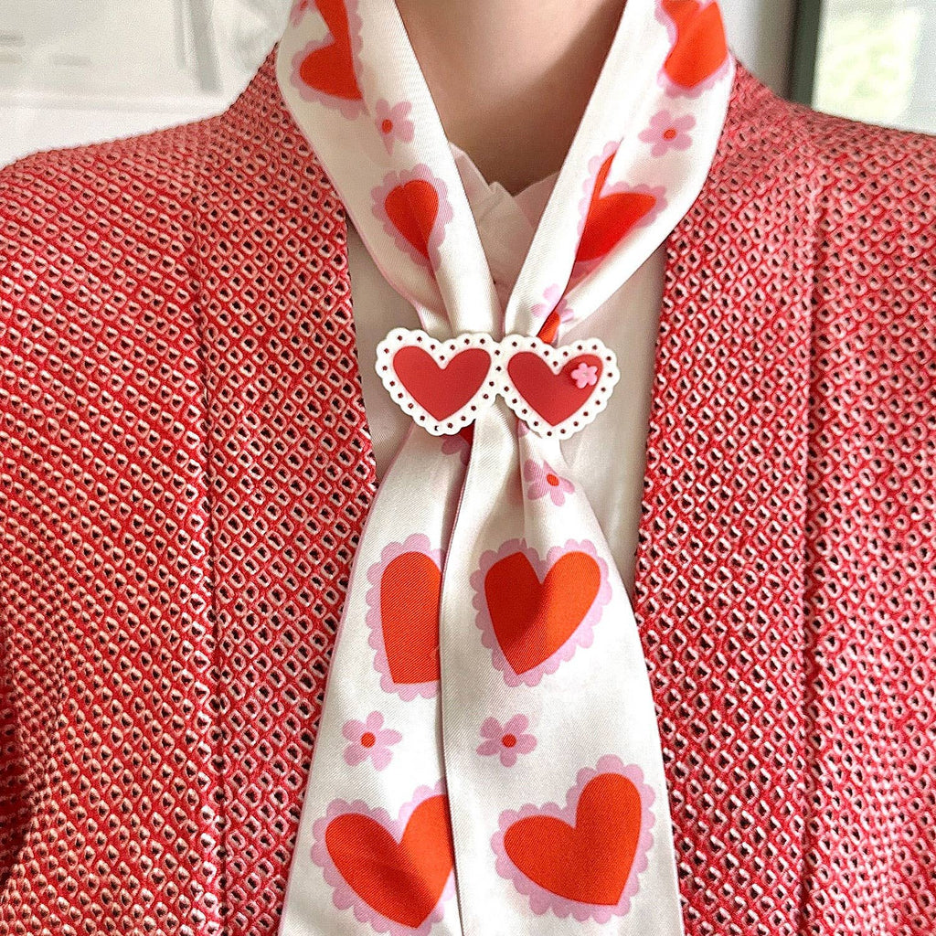 Person wearing a white scarf with red heart patterns over a red textured garment.
