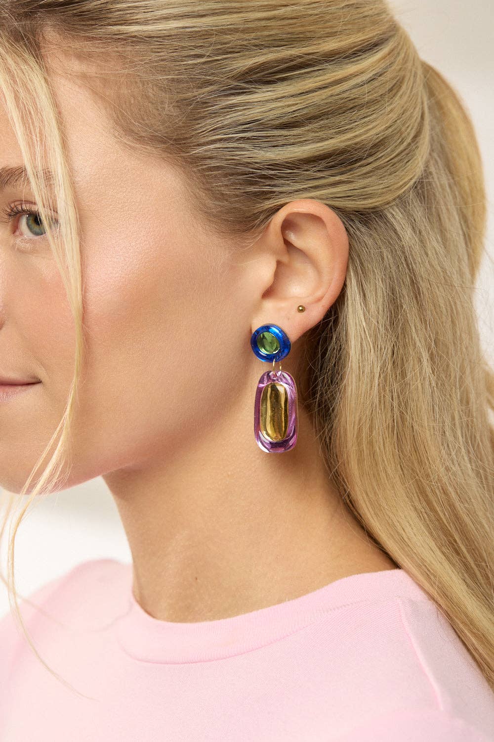 Close-up of a female presenting person wearing colorful earrings with a blurred background