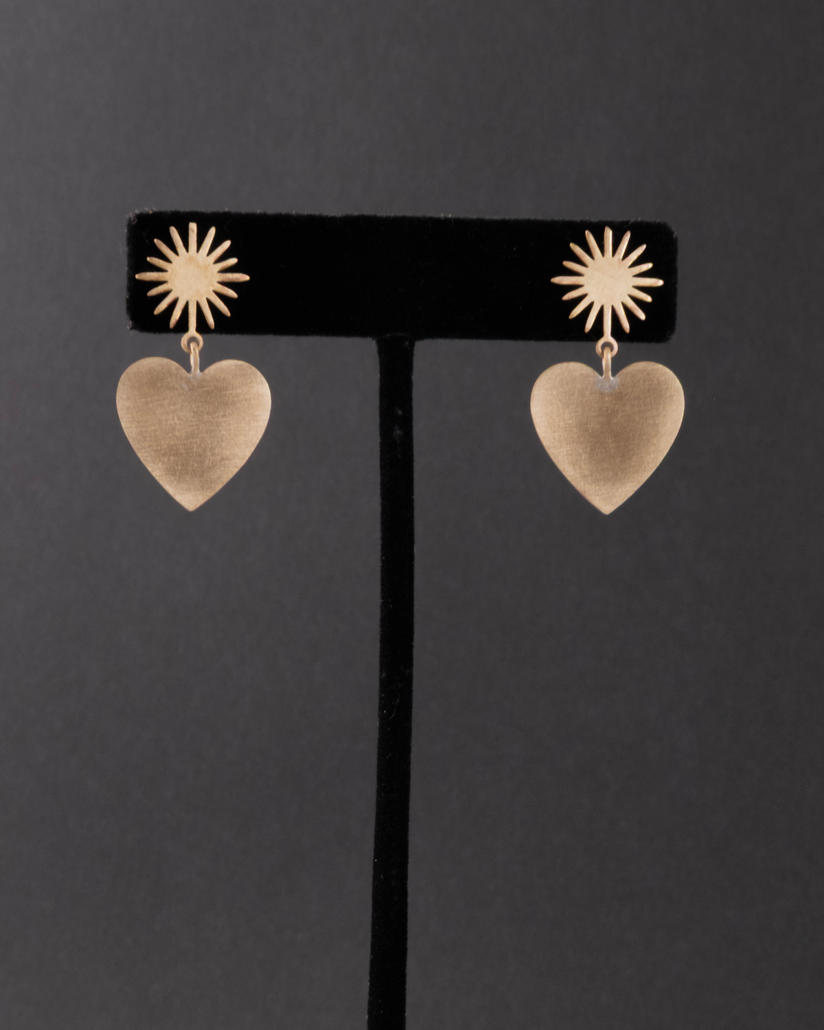 Heart-shaped earrings with starburst designs on a black stand against a dark background