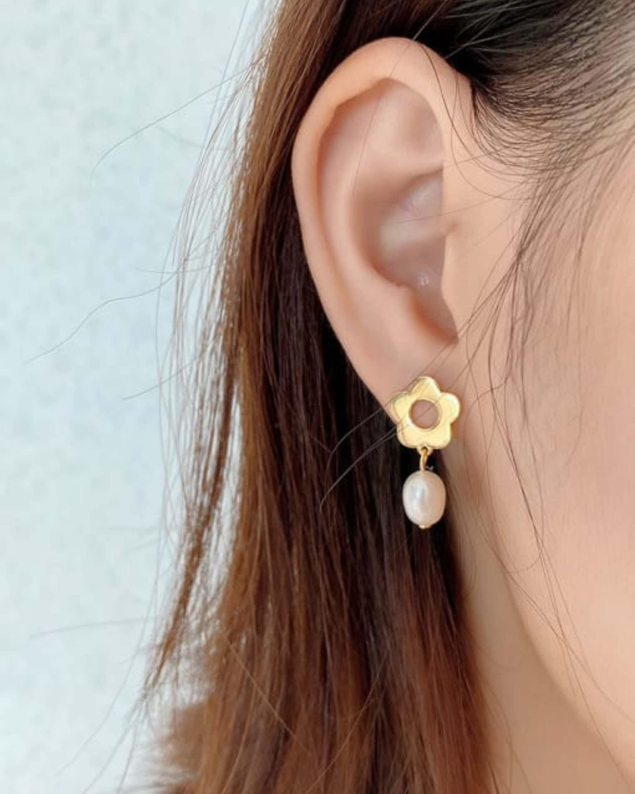 Gold earring with a pearl drop worn by a person against a light background