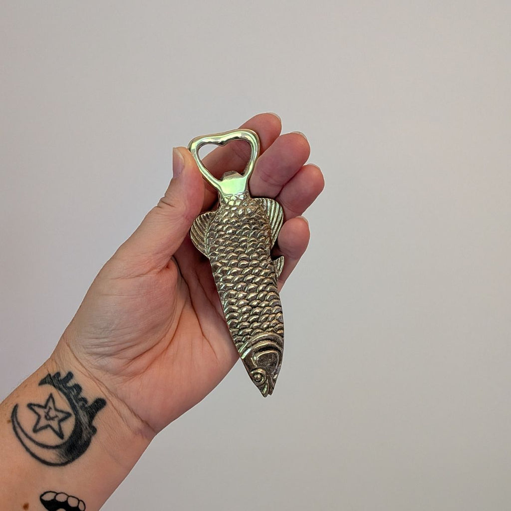Hand holding a fish-shaped bottle opener against a plain background