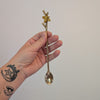 Hand holding a decorative gold spoon against a plain background
