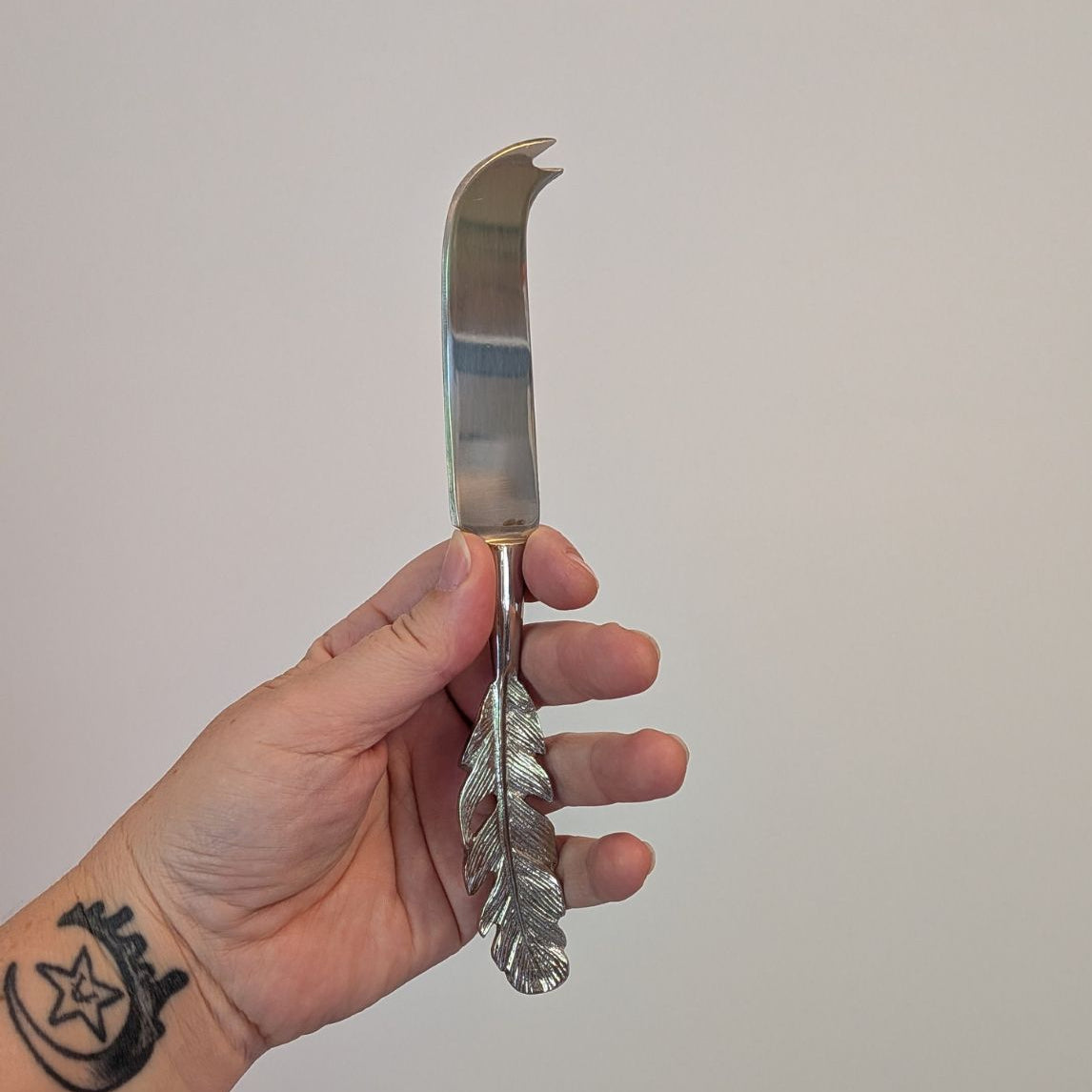 Hand holding a decorative silver cheese knife against a plain background