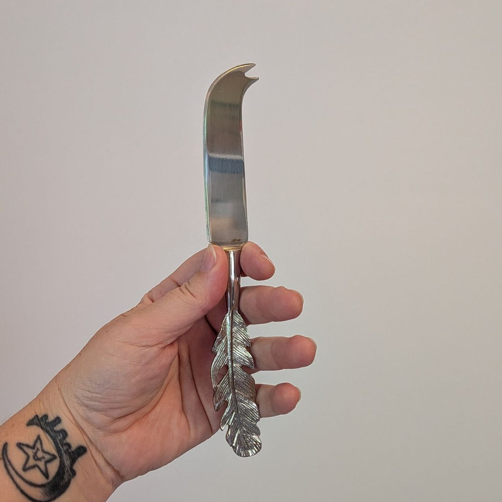 Hand holding a decorative silver cheese knife against a plain background