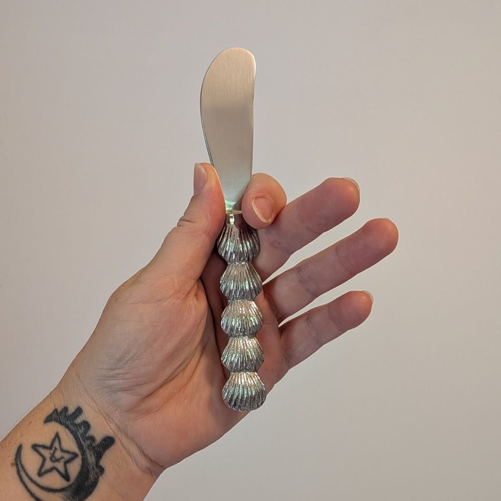 Hand holding a decorative knife with a shell pattern against a plain background