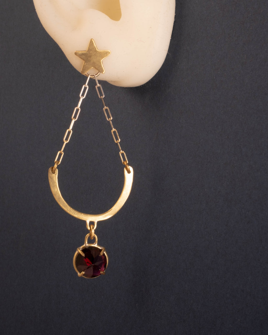 Gold earring with a star and red garnet gemstone on a dark background