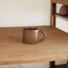 Brown ceramic mug on a wooden surface with a neutral background