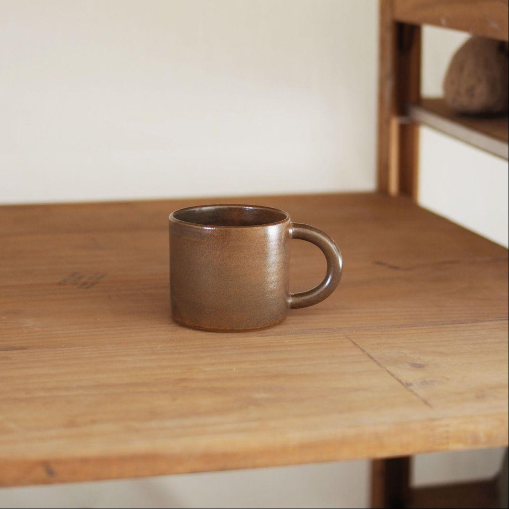 Brown ceramic mug on a wooden surface with a neutral background