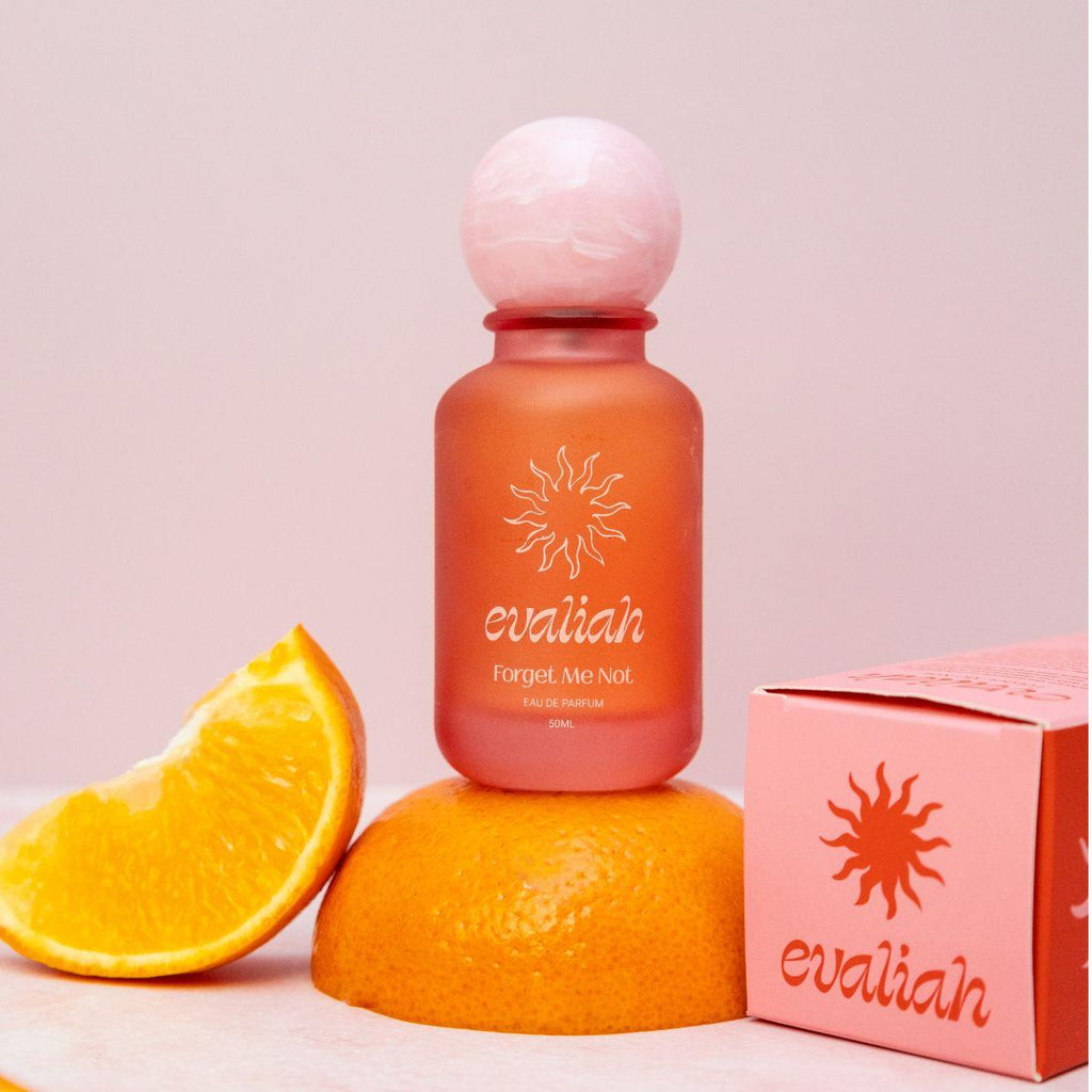 Evaliah perfume bottle and packaging on a pink background with an orange slice.