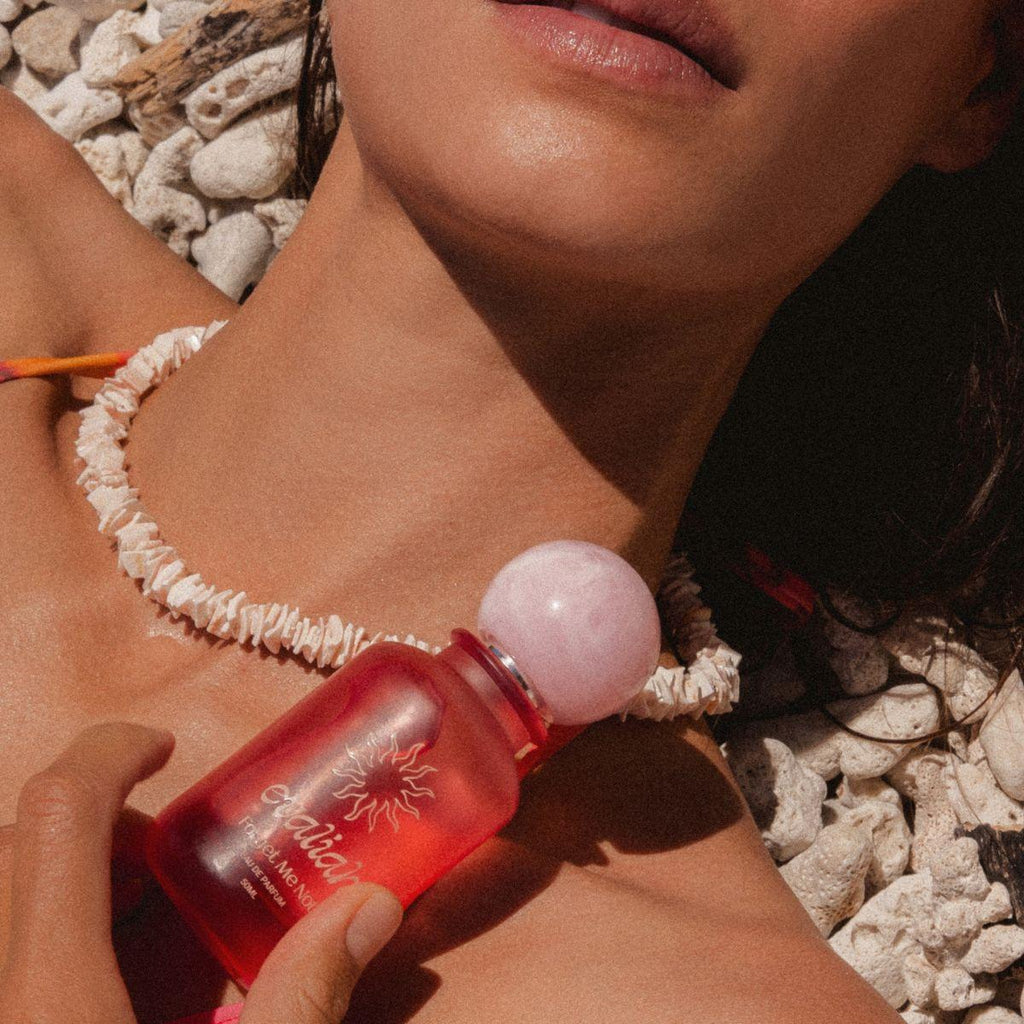 Person holding a red bottle with a pink cap on pebbles