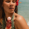 Woman holding a red bottle with a floral headband against a beach background