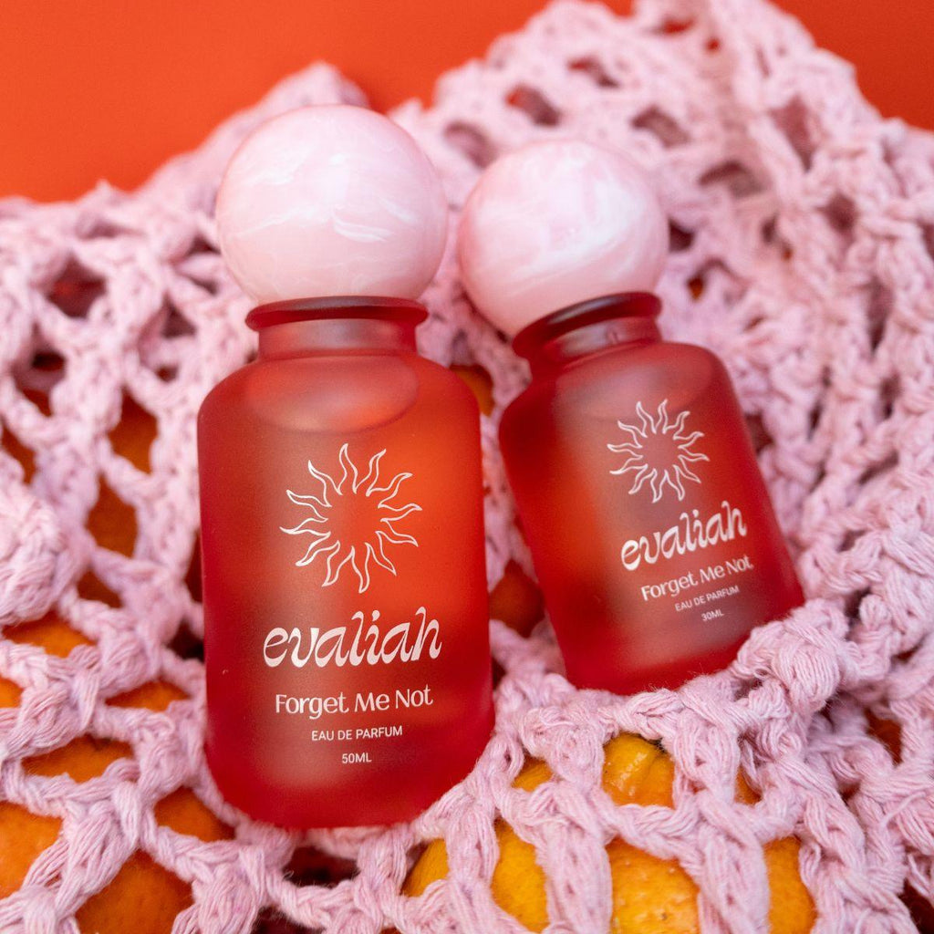 Two red perfume bottles labeled 'evaliah Forget Me Not' on a pink textured surface with an orange background.