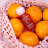 Red bottle with white cap labeled 'evaliah' surrounded by oranges in a pink textured bag.