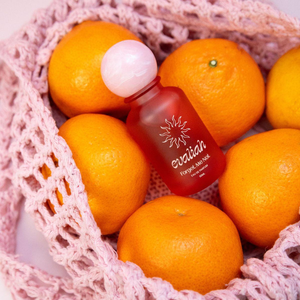 Red bottle with white cap labeled 'evaliah' surrounded by oranges in a pink textured bag.