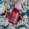 Red perfume bottle with pink cap on a bed of seashells and coral