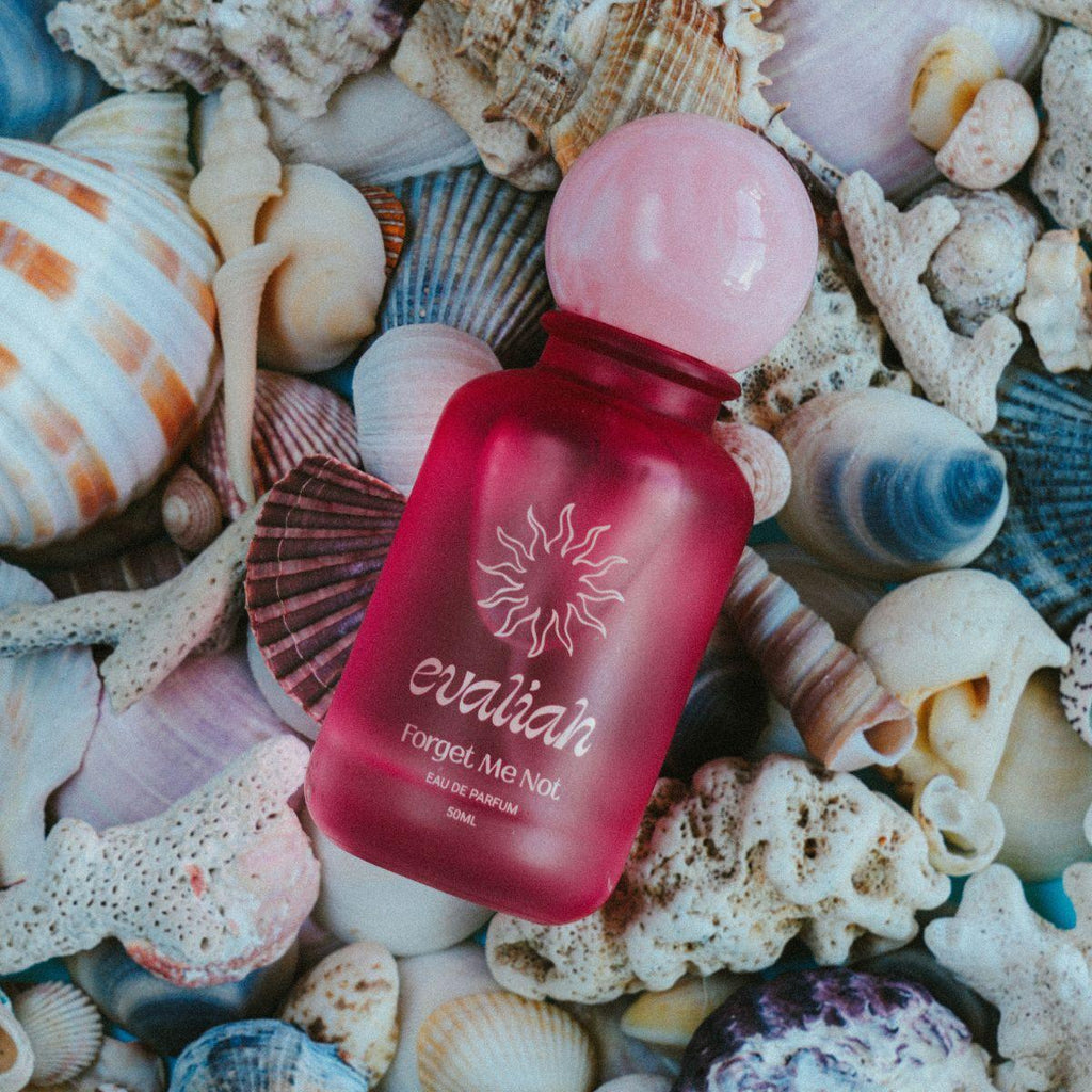 Red perfume bottle with pink cap on a bed of seashells and coral