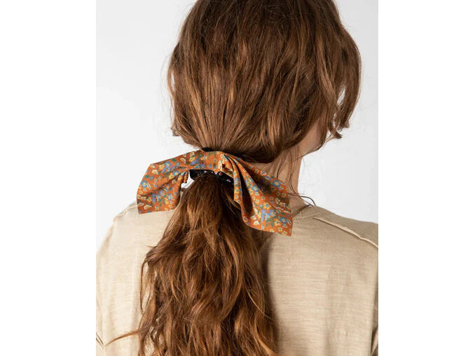 Person with a ponytail held by a floral scrunchie against a white background
