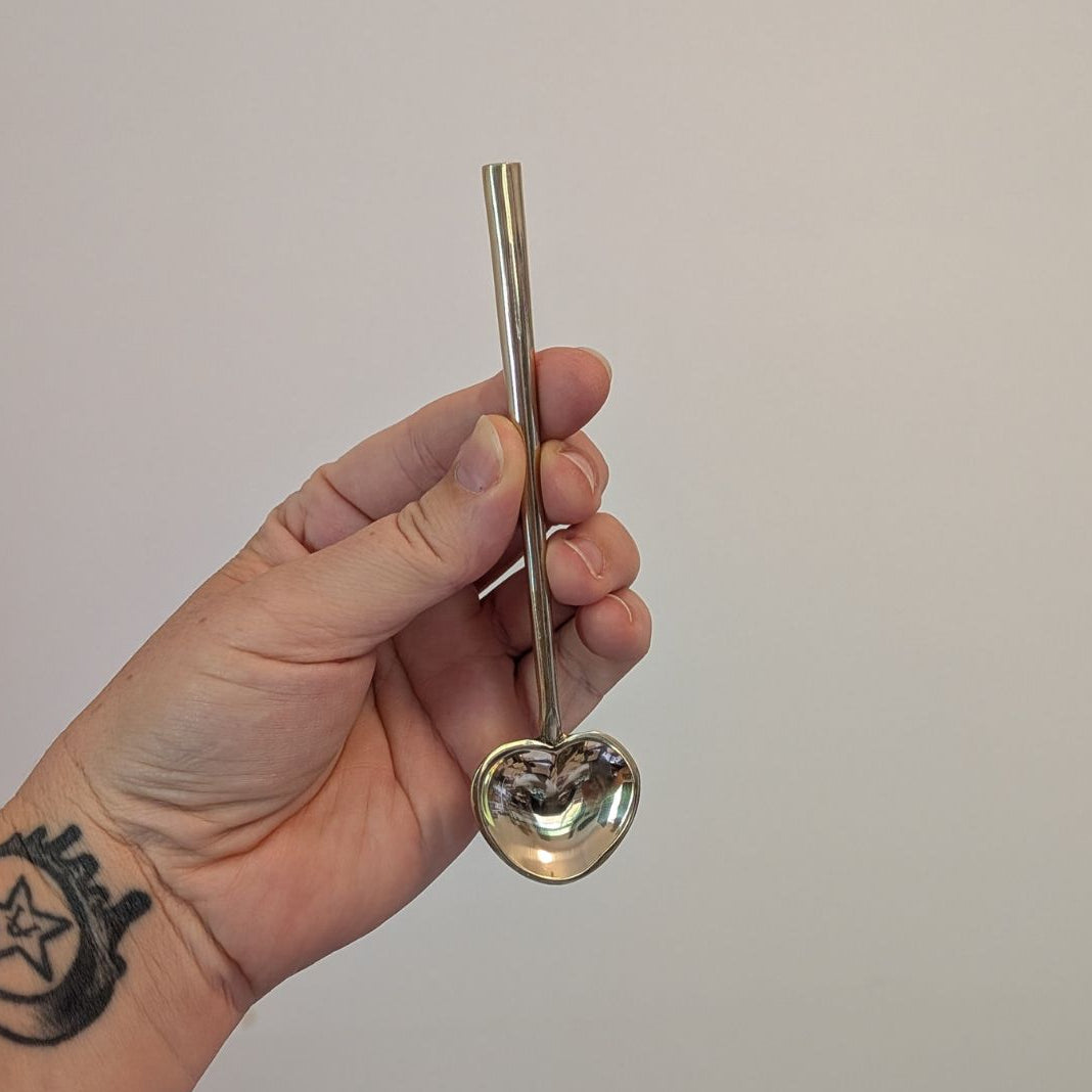 Hand holding a metal gold heart spoon  against a plain background