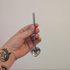 Hand holding a metal silver heart spoon against a plain background