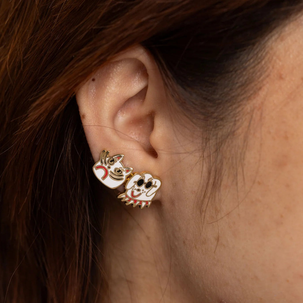 Close-up of an ear wearing gold earrings with cat and dog designs.