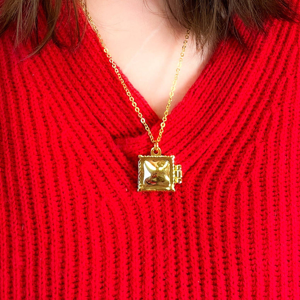 Gold ravioli locket necklace with a square pendant on a red sweater