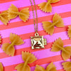 Gold necklace with a ravioli locket pendant on a pink and red striped background with bow-shaped pasta.