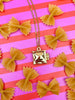 Gold necklace with a ravioli locket pendant on a pink and red striped background with bow-shaped pasta.
