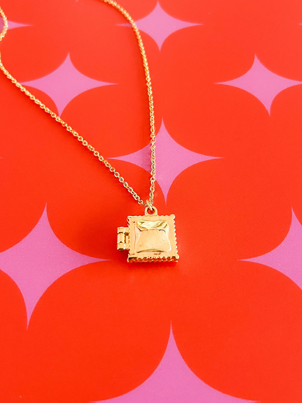 Gold necklace with a square Ravioli pendant locket on a red and pink patterned background