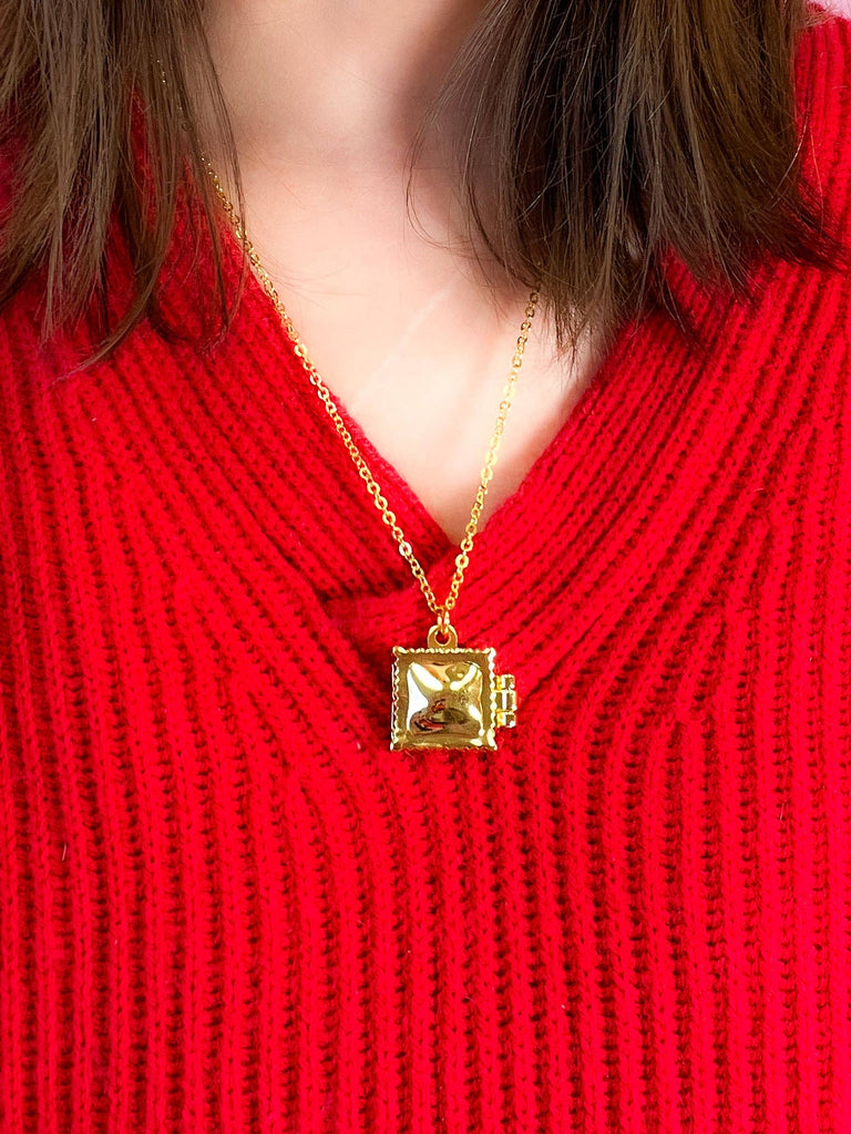 Gold ravioli locket necklace with a square pendant on a red sweater