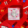 Small rectangular box with a cartoon character on a red background with dice and cards.